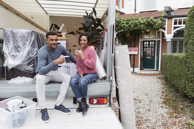 Portrait happy couple drinking tea, taking a break from moving at back of moving van — Stock Photo