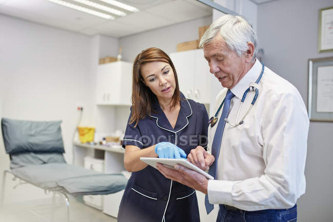 Médico y enfermera con tableta digital hablando en la sala de examen clínico - foto de stock