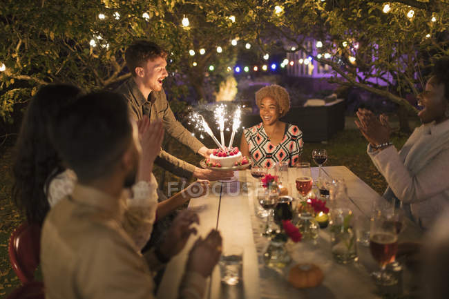 Happy friends celebrating birthday with sparkler cake at garden party table — Stock Photo