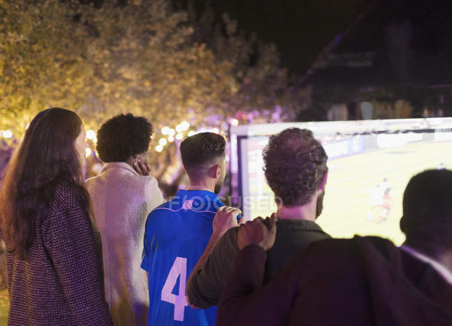 Друзья смотрят футбольный матч на проекционном экране во дворе — стоковое фото