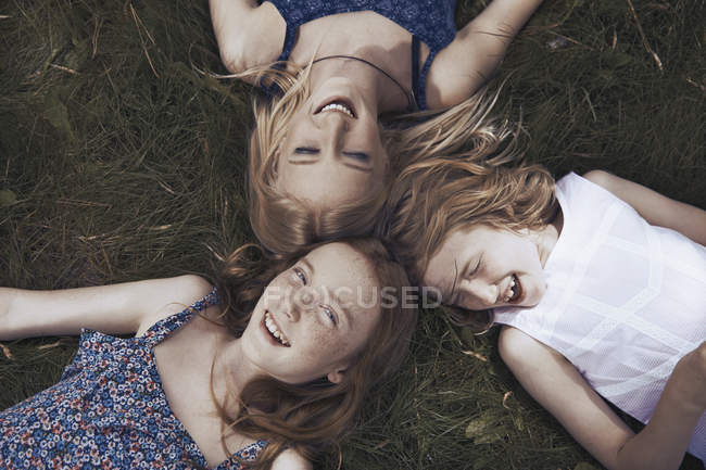 Retrato hermanas felices que yacen en la hierba - foto de stock