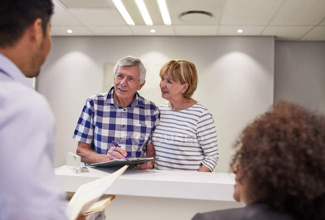 Seniorenpaar checkt ein, füllt Papiere an Klinik-Rezeption aus — Stockfoto