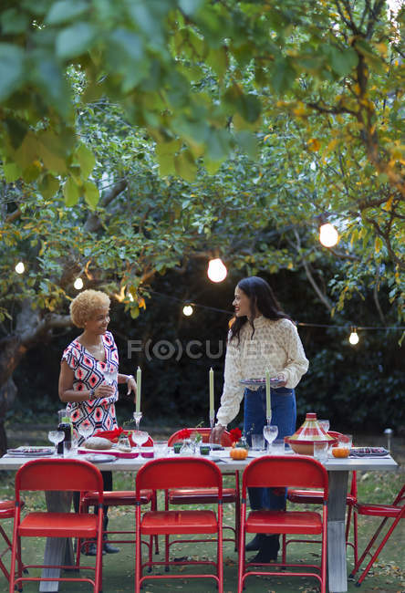 Mujeres amigas poniendo mesa para la cena fiesta en el jardín - foto de stock