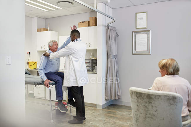 Médico examinando paciente masculino senior en sala de examen - foto de stock