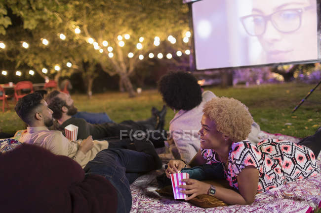 Friends relaxing, watching movie on projection screen in backyard — Stock Photo