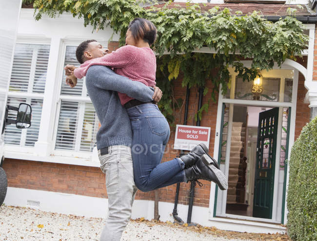 Feliz, pareja emocionada abrazando y celebrando fuera de casa nueva - foto de stock