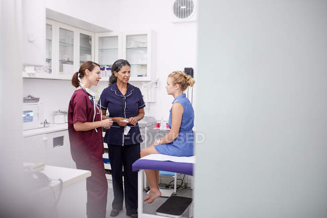 Female doctor and nurse talking to girl patient in clinic examination room — Stock Photo