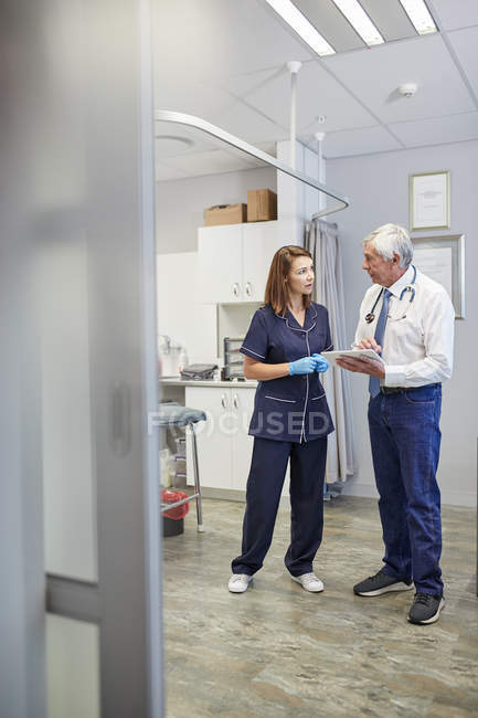 Médico y enfermera usando tableta digital en la sala de examen clínico - foto de stock