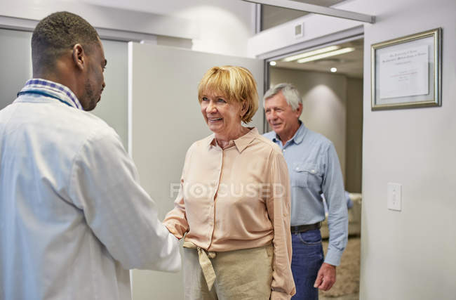 Doctor greeting senior couple in clinic doctors office — Stock Photo