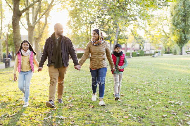 Familia musulmana cogida de la mano, caminando en el soleado parque otoñal - foto de stock