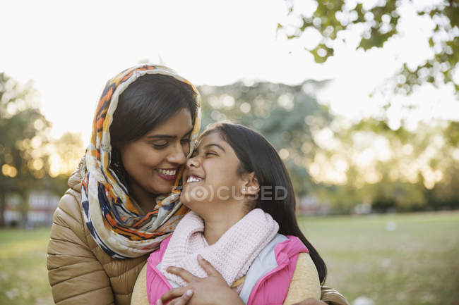 Cariñosa, feliz madre musulmana en hijab abrazando a su hija en el parque de otoño - foto de stock
