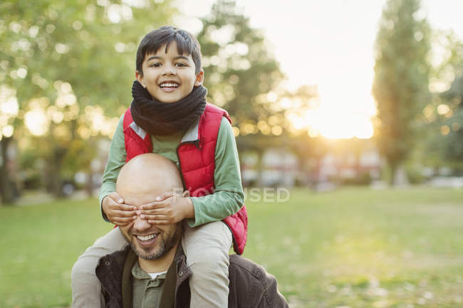Portrait playful son riding on fathers shoulders in autumn park — Stock Photo