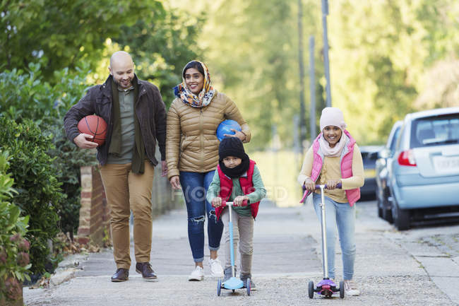 Familia musulmana viendo y montando scooter en la acera - foto de stock