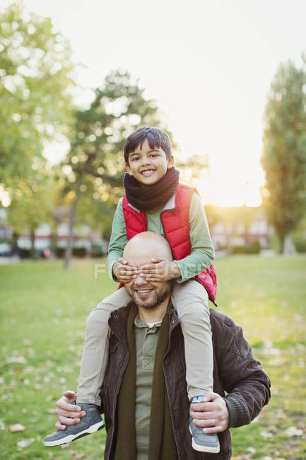 Portrait playful son riding on fathers shoulders in autumn park — Stock Photo