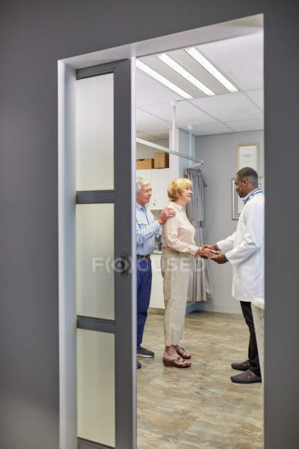Doctor shaking hands with senior couple in clinic examination room — Stock Photo
