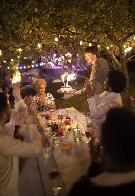 Friends celebrating birthday with sparkler cake at garden party — Stock Photo