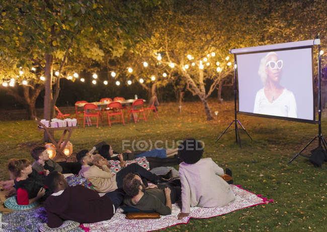 Friends watching movie on projection screen in backyard — Stock Photo