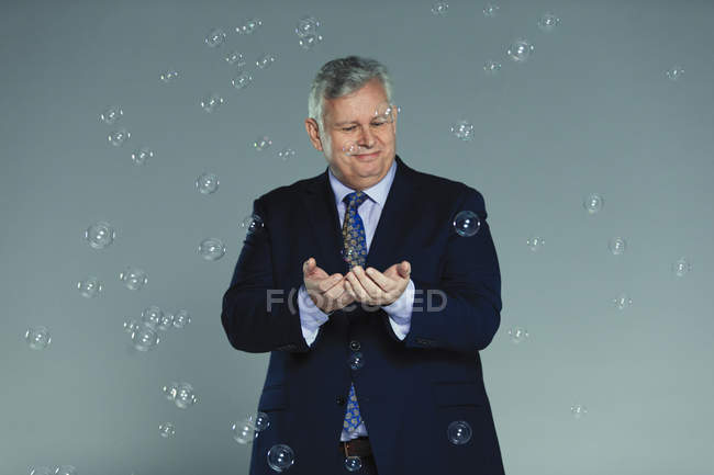 Homme d'affaires curieux et imaginatif attrapant des bulles qui tombent — Photo de stock