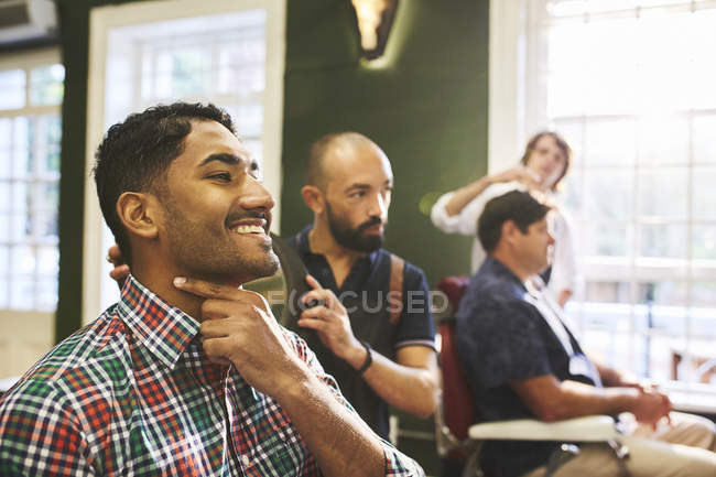 Sonriente cliente masculino comprobando la cara afeitada en la barbería - foto de stock