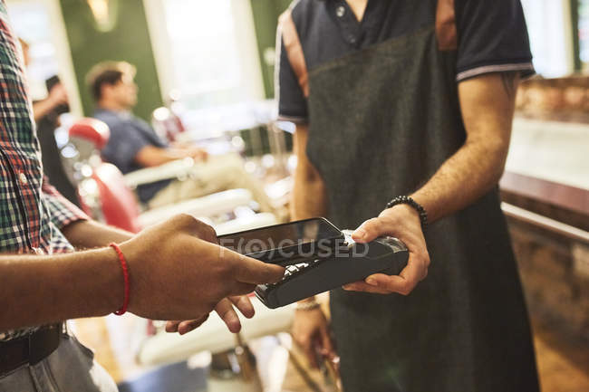 Male customer paying barber with smartphone contactless payment in barbershop — Stock Photo