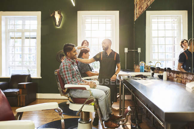Barbeiros masculinos e clientes em barbearia — Fotografia de Stock