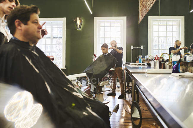 Clientes masculinos y peluqueros en barbería - foto de stock