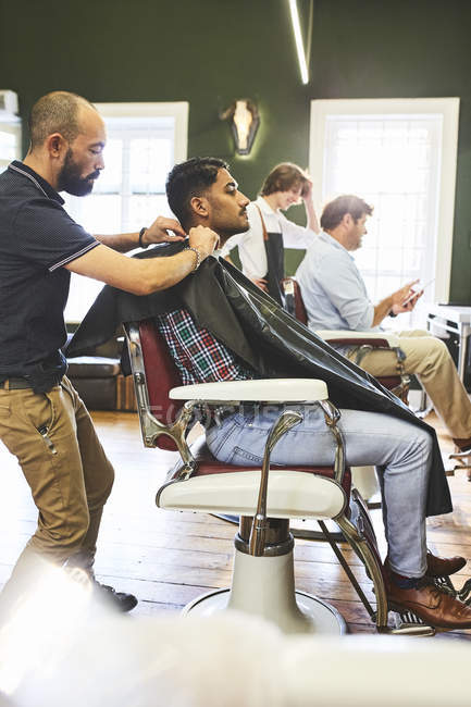 Barbeiro masculino preparando cliente para corte de cabelo na barbearia — Fotografia de Stock