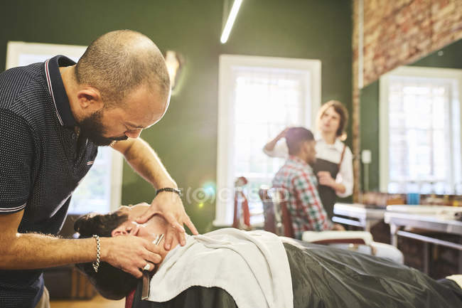 Чоловічий перукар гоління обличчя клієнта в перукарні — стокове фото