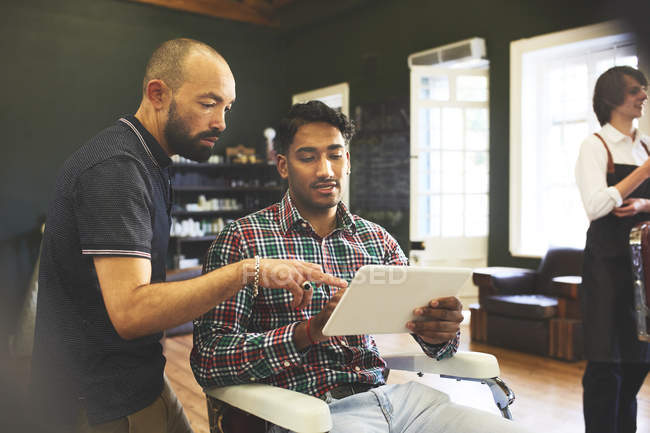 Мужчина парикмахер и клиент с цифровой планшет говорить в парикмахерской — стоковое фото