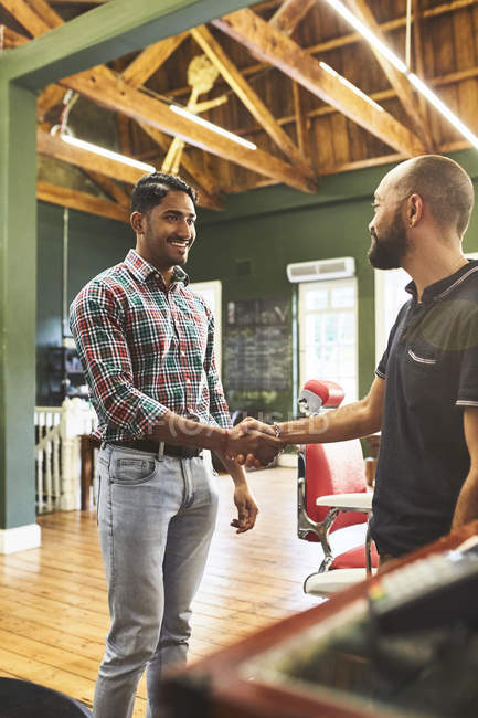 Male barber and customer shaking hands in barbershop — Stock Photo