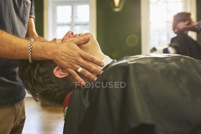 Мужчина парикмахер массажное лицо клиента в парикмахерской — стоковое фото