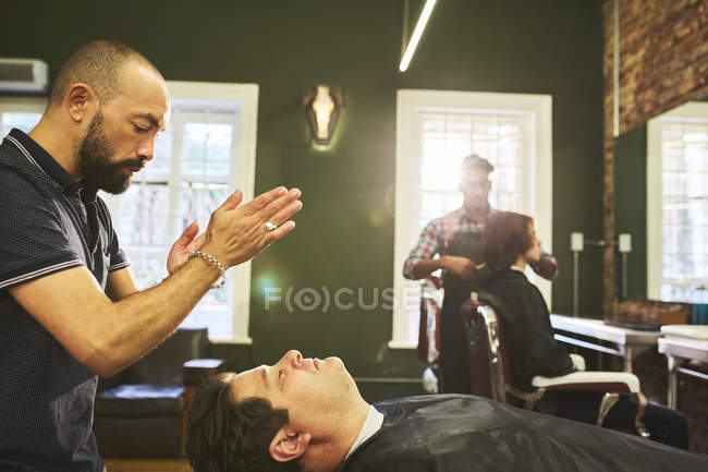 Barbeiro masculino em pé sobre o cliente na barbearia — Fotografia de Stock