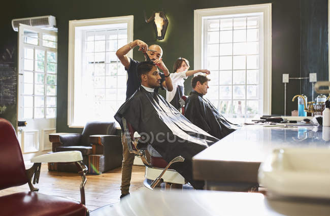 Barbieri maschi che tagliano capelli di clienti in negozio di barbiere — Foto stock