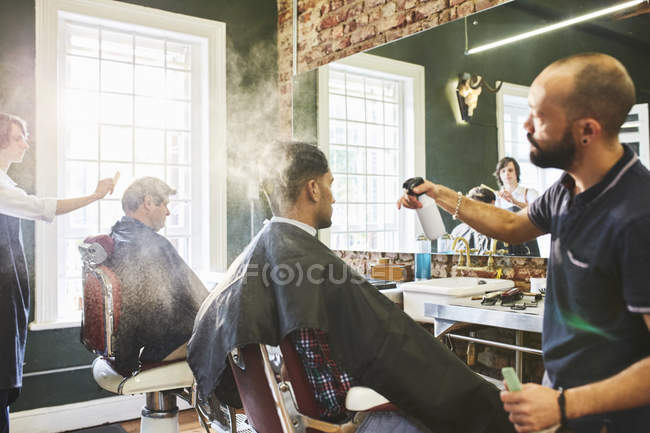 Peluquería masculina rociando el cabello del cliente en la barbería - foto de stock