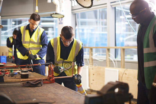 Male instructor watching students welding in workshop — Stock Photo