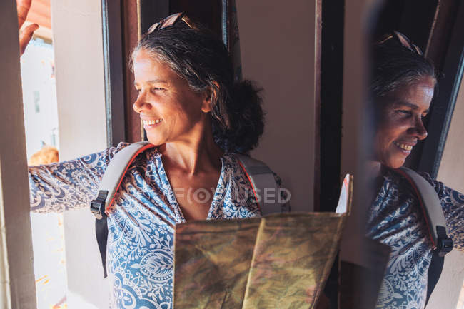 Sorrindo turista feminina com mapa olhando para a janela ensolarada — Fotografia de Stock