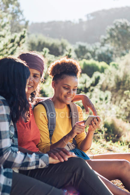 Mother and daughters using smartphone, hiking in sunny woods — Stock Photo