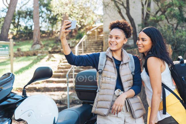 Felices jóvenes amigos tomando selfie con el teléfono de la cámara en el scooter - foto de stock