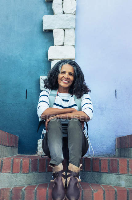 Портрет улыбающейся, уверенной женщины, сидящей на кирпичных ступенях — стоковое фото