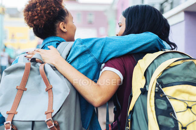 Visão traseira de jovens amigos afetuosos com mochilas abraçando — Fotografia de Stock
