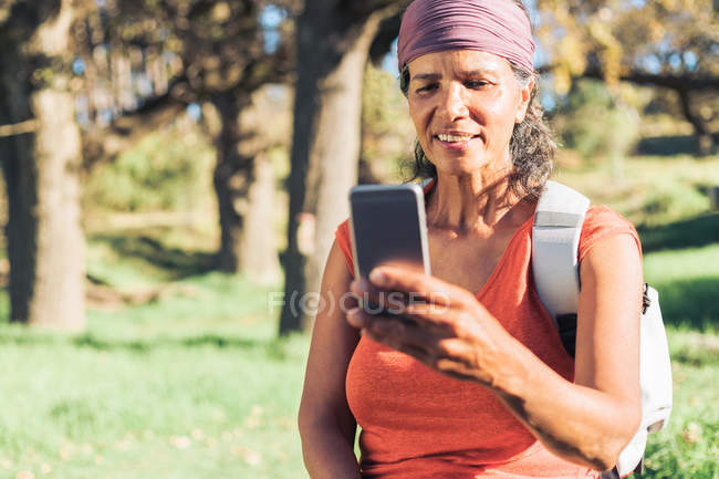 Caminhante feminino usando smartphone em madeiras ensolaradas — Fotografia de Stock