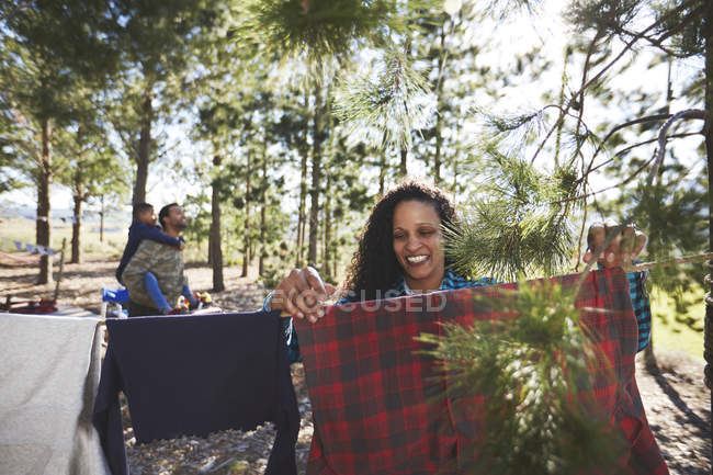 Smiling woman hanging clothing on campsite clothesline in woods — Stock Photo