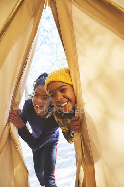 Playful brother and sister peeking into camping teepee — Stock Photo