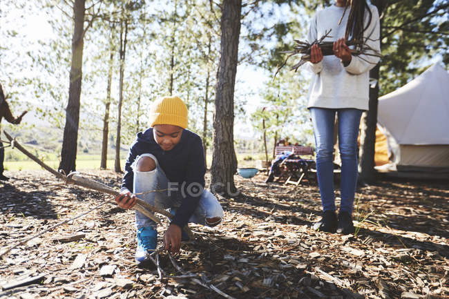 Boy picking up sticks for firewood at sunny campsite in woods — Stock Photo