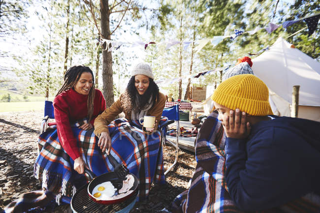 Lesbian couple and kids cooking breakfast at campsite grill in woods — Stock Photo