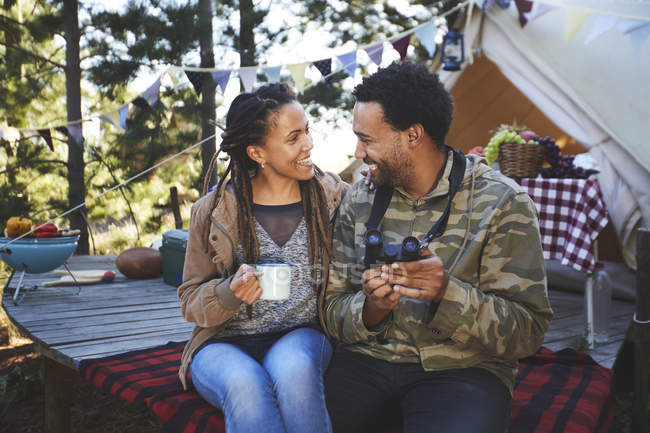 Casal jovem afetuoso com binóculos bebendo café no acampamento — Fotografia de Stock
