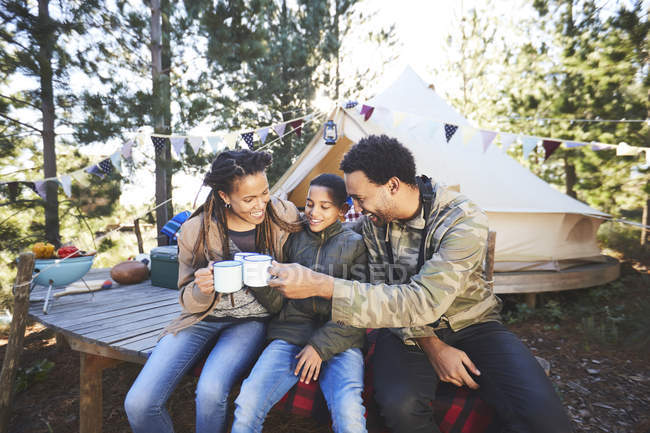 Happy family drinking coffee and hot chocolate at campsite in woods — Stock Photo