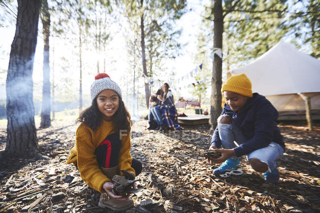 Portrait of smiling girl gathering kindling at sunny campsite in woods — Stock Photo