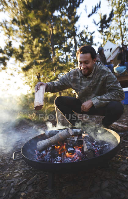 Homme ajoutant du bois de chauffage au feu de camp du camping — Photo de stock