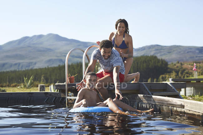 Feliz familia nadando en la soleada piscina de verano - foto de stock
